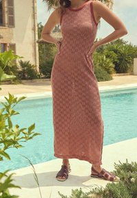 Robe maxi à rayures rouges et blanches avec une texture côtelée et une coupe sans manches ; associée à des sandales à lanières marron, installée au bord d'une piscine.