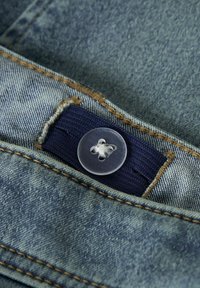 Denim tkanina svetlo modre barve, ki vsebuje prozoren gumb z cvetličnim vzorcem in temno modrim trakom, poudarjena z rjavim šivom.