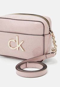 Mała różowa torebka na ramię z tłoczonym wzorem CK, złotym logo CK na przodzie, zamkiem błyskawicznym na górze oraz odpinanym paskiem z detalem ze złotego łańcuszka.
