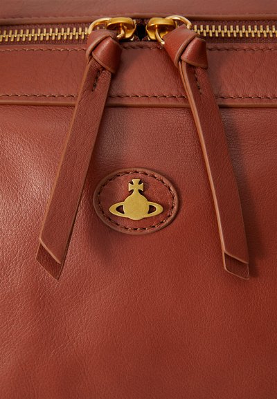 Brown leather bag with a smooth texture, featuring gold hardware, a zip closure, and a logo embossed on a circular patch.