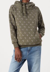 Sweat à capuche vert olive en tissu doux avec un col à capuche à cordon. Présente un motif répétitif de petites formes d'éventail rouges et bleues. Coupe décontractée.