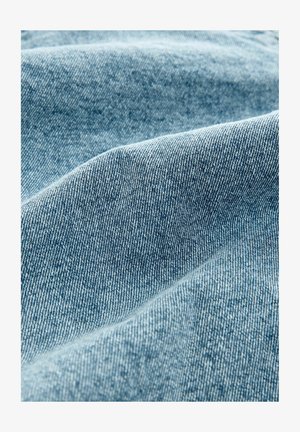 Vaaleansininen farkkukangas, jossa on kuitupinta; pehmeä, hieman venynyt, näkyvillä ompelujäljillä ja sileällä pinnalla.