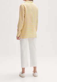 Lightweight, collared shirt in pastel yellow with thin horizontal stripes, paired with cropped white trousers and white sneakers.