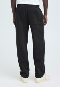 Schwarze Sweatpants mit lockerem Schnitt, ausgestattet mit einem elastischen Bund und einer Gesäßtasche. Weicher Stoff mit minimalen Nähdetails.