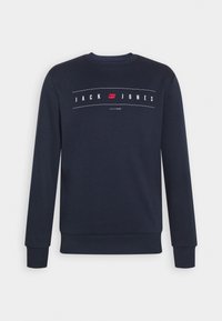 Sweat-shirt bleu marine à manches longues avec le texte « JACK JONES » et un logo rouge centré entre de fines lignes horizontales blanches.