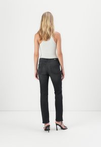 Jeans negri din denim cu croială dreaptă, cinci buzunare și talie medie. Purtate cu un maiou gri deschis și tocuri negre.