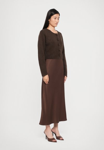 Brown knitted cardigan with round neckline and front buttons, layered over a brown satin slip dress; model wearing open-toed brown heels.