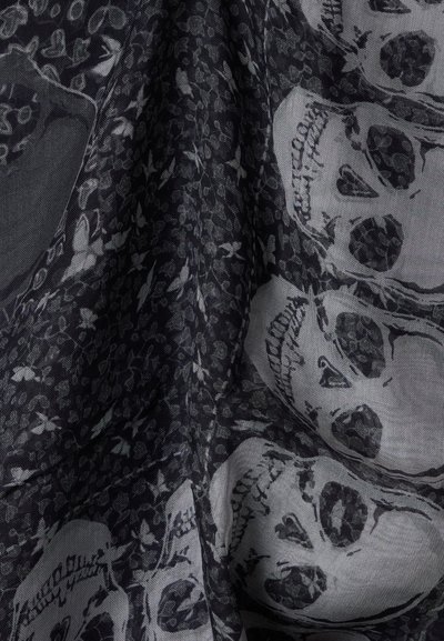 Σκούρο ύφασμα με μοτίβο από λευκά κρανία και μικρά ανθισμένα σχέδια, που δείχνει πτυχώσεις και υφή.