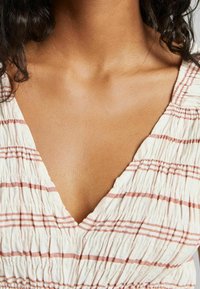 Abito di tessuto bianco con sottili strisce rosa, caratterizzato da una profonda scollatura a V e una texture arricciata attorno al collo e alle spalle.