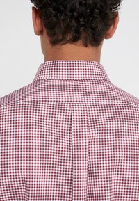 Lockig person som bär en röd och vit rutig skjorta, sedd bakifrån, med fokus på kragen och övre ryggen.