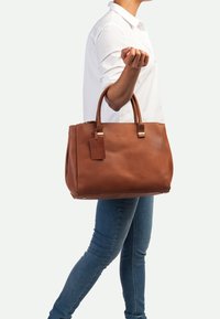 Bruine leren handtas met gestructureerd ontwerp, dubbele handvaten, accenten in gouden tint en een afneembare tag. Gladde textuur, rechthoekige vorm.