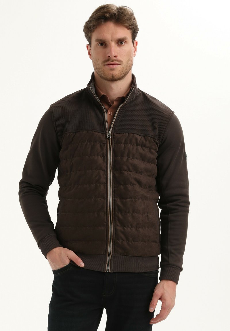 Bruine zip-up jas met een geborduurde voorkant, geribbelde schouderontwerpen en gebreide mouwen. Het materiaal is glad met een matte afwerking.