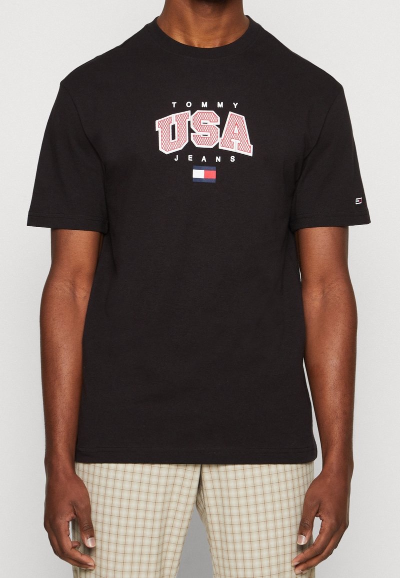 Black cotton t-shirt featuring a white and red "USA" graphic and "TOMMY JEANS" text. Includes a small logo by the sleeve.