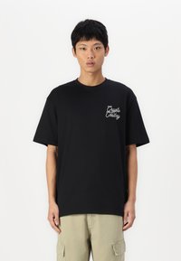 Sort bomulds t-shirt med et design i hvid skrift på venstre bryst. Kortærmet, rund hals, afslappet pasform, ensartet tekstur.