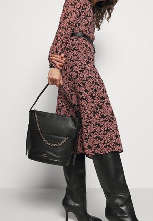 Mujer con un vestido negro con flores rosas que lleva botas negras de tacón hasta la rodilla, sosteniendo un bolso de cuero negro con un detalle de cadena.