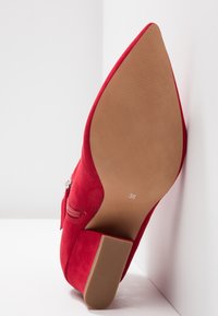 Czerwone zamszowe szpilki z ostro zakończonym noskiem i fakturowaną beżową podeszwą. Zawierają detal w postaci zamka błyskawicznego i oznaczoną rozmiar 38 na wkładce.