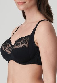 Mustan langattoman rintaliivin läpinäkyvät pitsikupit, joissa on kukkakuvioita, aallotetut reunat ja teksturoitu kangas. Säädettävät olkaimet ja hakaskiinnitys.