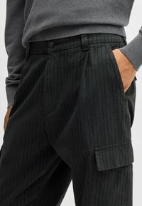 Czarne spodnie cargo w paski o teksturowanym wykończeniu, z kieszenią boczną i luźnym krojem. Guziki w talii.