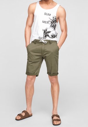 Weißes Tanktop mit schwarzem Text und Palmenmotiv. Olivgrüne Shorts mit umgeschlagenen Säumen. Braune Sandalen mit Riemen und Schnallen.