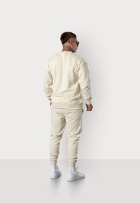 Sweat-shirt de couleur crème et joggers assortis en matériau doux. Comprend des poignets côtelés, des poches latérales et un petit logo dans le dos.