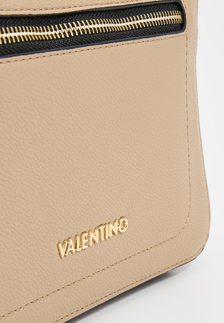Beige strukturiertes Lederhandtasche mit einem goldenen Reißverschluss und Logodetail. Das Design umfasst einen schwarzen Reißverschlussakzent an der Oberseite.