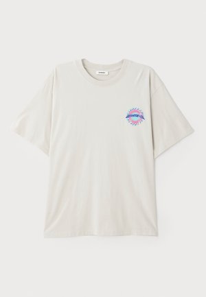 Beige bomull t-skjorte med rund hals og korte ermer. Har en flerfarget grafisk logo på venstre brystområde. Glatt tekstur.