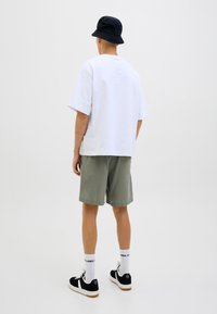 Camiseta de algodón blanca, de corte holgado, combinada con pantalones cortos verdes oliva. Sombrero cubo negro, zapatillas negras y blancas, calcetines blancos con logo.