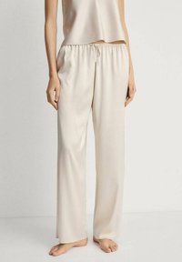 Bež, lagane hlače opuštenog kroja s elastičnim pojasom i vezicom. Glatka tekstura, punog kroja, pogodne za svakodnevno nošenje.