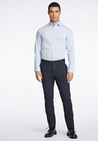 Camicetta azzurro chiaro a maniche lunghe con colletto a bottoni, abbinata a pantaloni neri scuri e scarpe nere, che mostrano un design aderente.