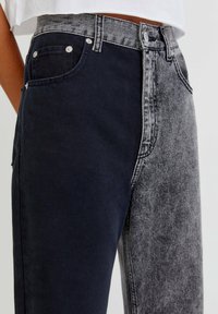 Jeans bicolor con tejido azul oscuro en un lado y gris desgastado en el otro, con costuras en contraste y diseño de bolsillo tradicional.