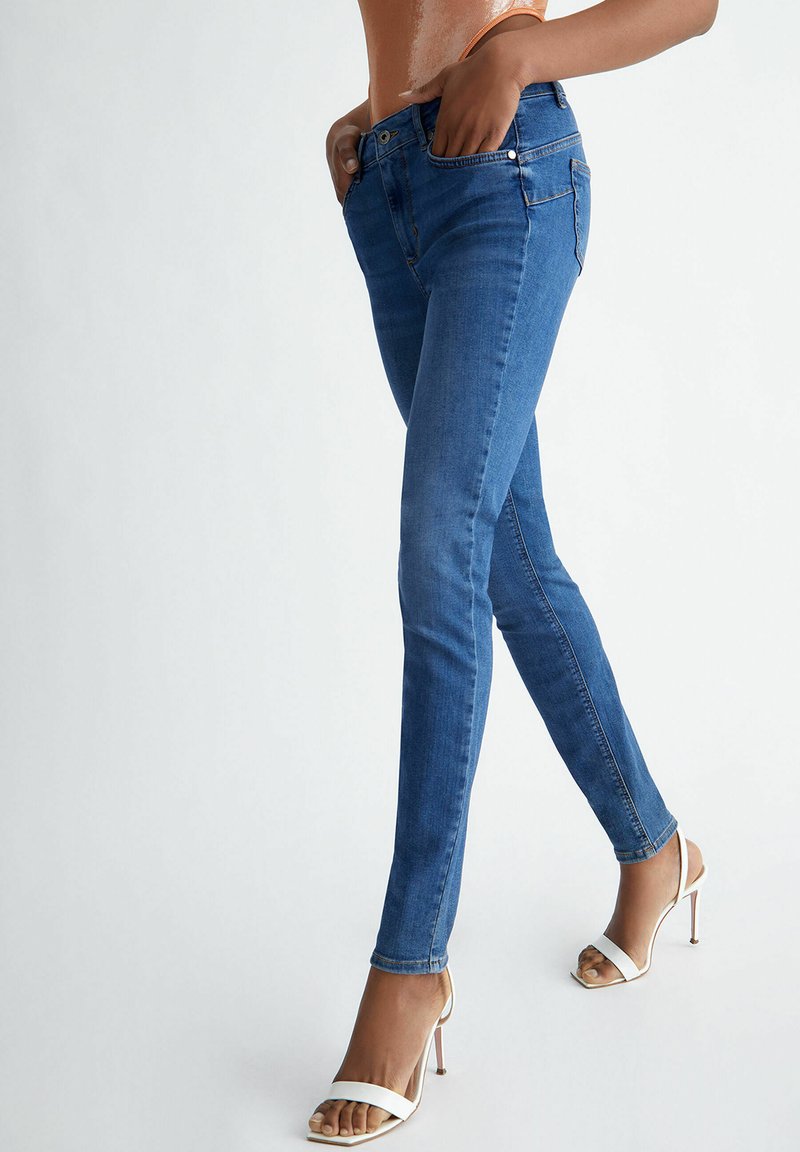 Jeans skinny en denim avec une texture lisse, présentant une taille haute, cinq poches et des détails de couture subtils.
