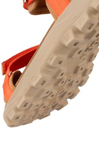 Oranssi säädettävä hihnasandaali, jossa on ruskea nahkainen päällinen ja beige kumipohja, jossa on teksturoitu pinta ja neliömäinen kuvio.