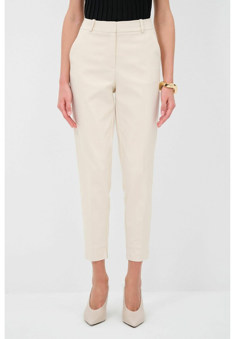 Beige kalhoty na míru s vysokým pasem, slim fit a nohavicemi do kotníků. Hladká tkanina a minimální detaily. Spárováno s béžovými podpatky.