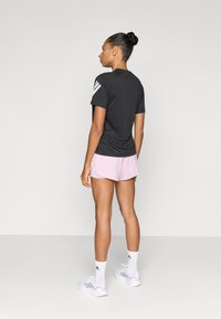 Zwart atletisch T-shirt met korte mouwen en drie witte strepen op de rechterschouder, gecombineerd met roze korte broek en witte sneakers.