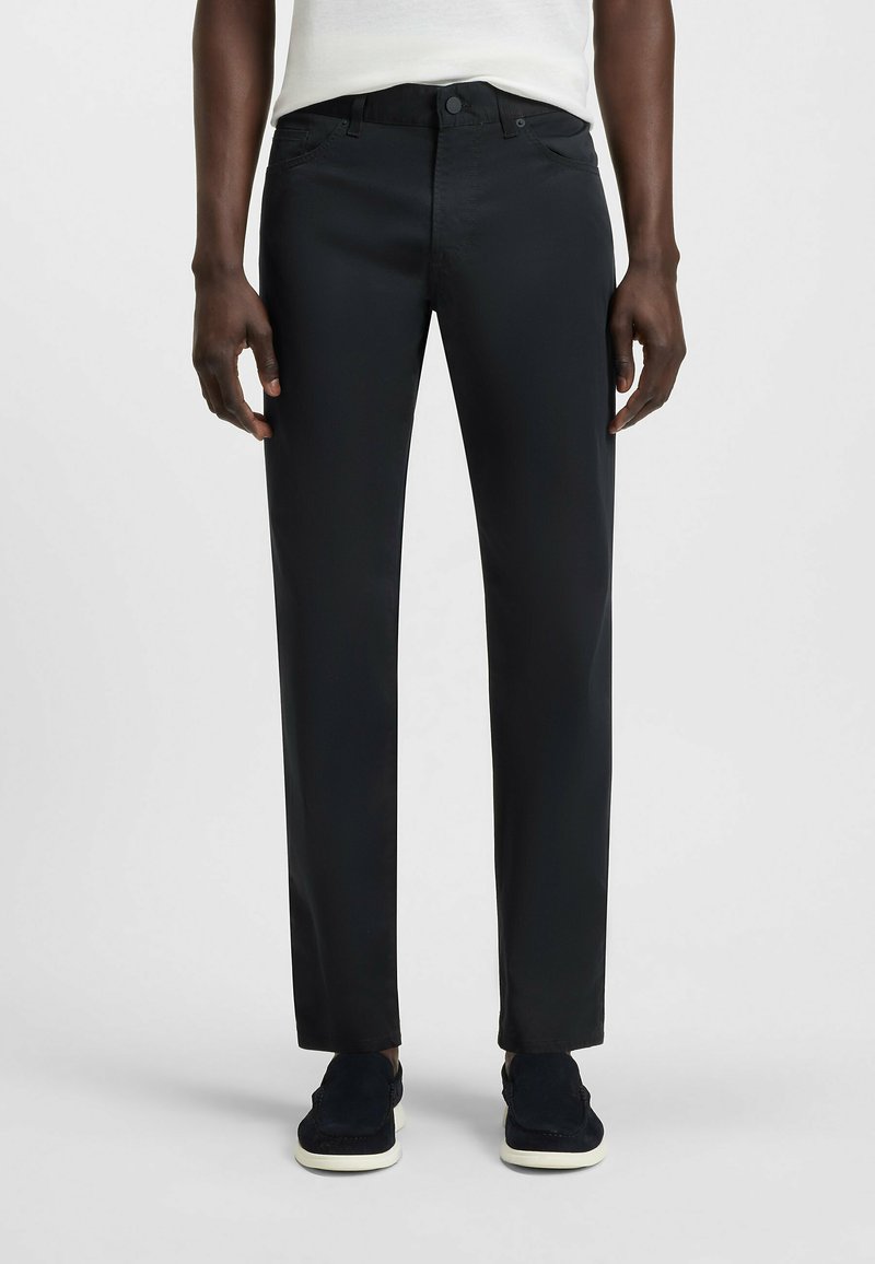 Zwarte, rechte broek met een gladde textuur, gemaakt van een lichtgewicht stof. Voorzien van zijzakken, een knoopsluiting en riemlussen.