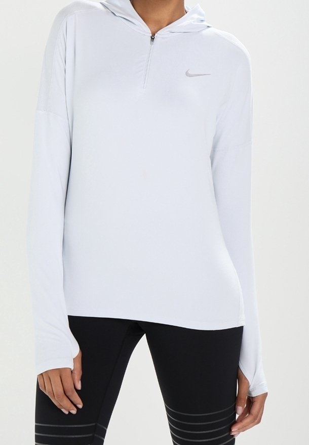 Felpa Nike bianca a maniche lunghe con design a mezza zip, texture morbida e logo discreto. Abbinata a leggins sportivi neri con righe.