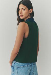 Haut sans manches vert avec un col marine, fabriqué dans un tissu lisse. Il présente une coupe décontractée et un ourlet arrondi, associé à un short en denim bleu clair.
