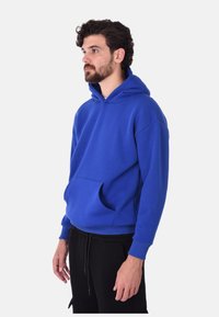 Felpa blu con cappuccio in una vestibilità comoda, dotata di tasca frontale e polsini a costine. Realizzata in tessuto spesso e liscio con una consistenza morbida.