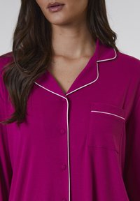Rosa randig pyjamaskjorta med vit piping, med en notch-krage, knappstängning fram och en bröstficka med dekorativ accent.