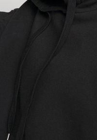 Zwarte hoodie met een gestructureerd oppervlak. Bevat trekkoorden, een voorzak en versterkte stiksels.