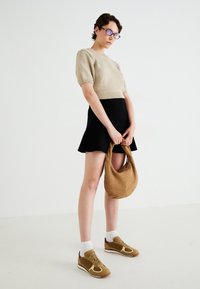 Beige gestrickter Kurzarmpullover, schwarzer ausgestellter Minirock, hellbraune gewebte Handtasche und braune Turnschuhe mit weißen Akzenten und Socken.