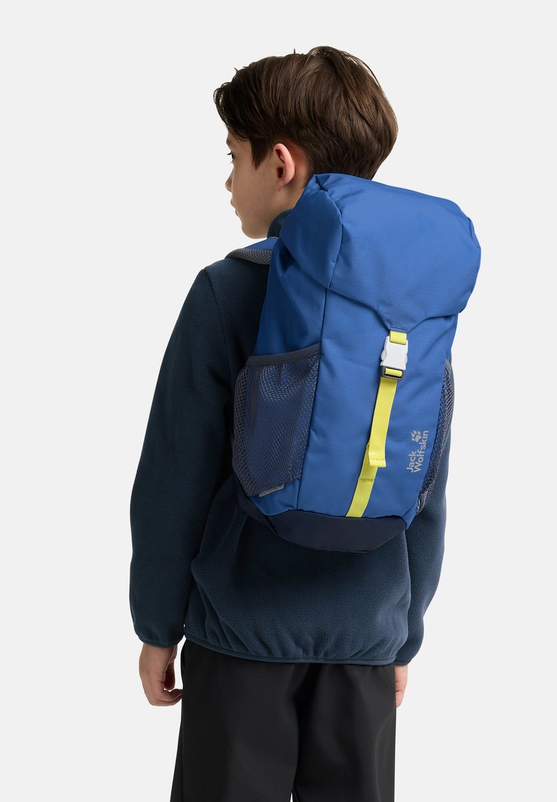 Kind, seitlich blickend, trägt einen blauen Rucksack mit gelbem Riemen und seitlichen Netzfächern, gekleidet in eine dunkelblaue Fleecejacke.