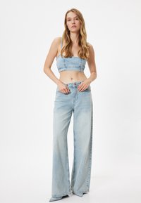 Vaaleansininen denimcrop-top, jossa on ohuet olkaimet, yhdistettynä leveisiin vaaleansinisiin farkkuihin, joissa on korkea vyötärö ja etupainike.