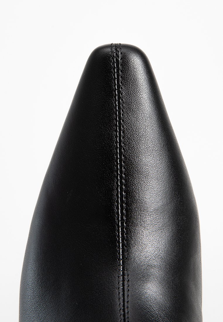 Scarpa di pelle nera con punta affusolata e dettagli di cucitura visibili. Texture liscia con una finitura lucida e un design elegante.