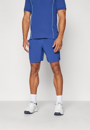 Blauwe atletische polo met contrasterende lichtblauwe stiksels, gecombineerd met bijpassende shorts. Witte sneakers met marineblauwe accenten maken de outfit compleet.