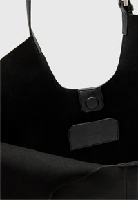 Černá semišová taška přes rameno s velkým otvorem, vybavená koženou štítkem a patentním uzávěrem. Hladký povrch bez viditelných vzorů.