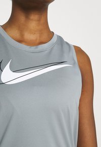 Débardeur de sport gris avec design sans manches, arborant un grand logo Nike blanc et des accents noirs à l'avant. Tissu lisse et léger.