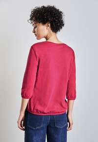 Magenta top s tříčtvrtečními rukávy, kulatým výstřihem a elastickým pasem. Bavlna nebo podobný materiál, hladká textura, ležérní styl.