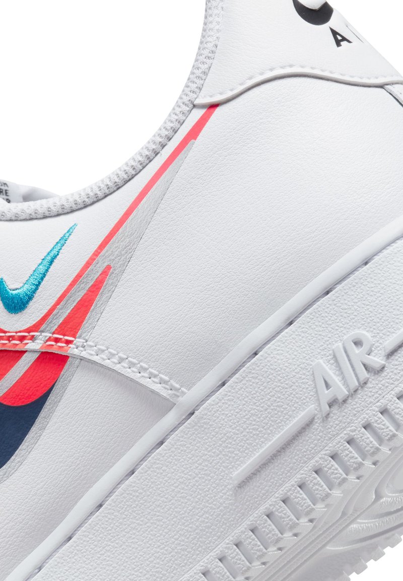 Białe skórzane sneakersy z turkusowymi i czerwonymi akcentami, posiadające teksturowaną podeszwę, przeszycia oraz wypukłe logo "AIR" z boku.