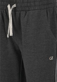 Mörkgrå sweatpants gjorda av mjukt tyg med en texturerad yta. Har en elastisk midja, sidfickor och en vit snörning.